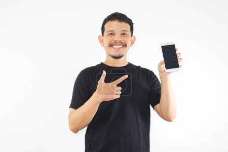 Foto de Adulto asiático hombre sonriendo feliz mientras muestra la pantalla del teléfono móvil en blanco y apuntando a ella - Imagen libre de derechos