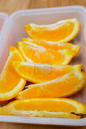 Téléchargez les photos : Fruits orange Sunkist dans un récipient en plastique sur une table en bois - en image libre de droit
