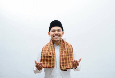 Asian Muslim man wearing white clothes  and sarung smiling to give greeting during Ramadan and Eid Al Fitr celebration standing over white background