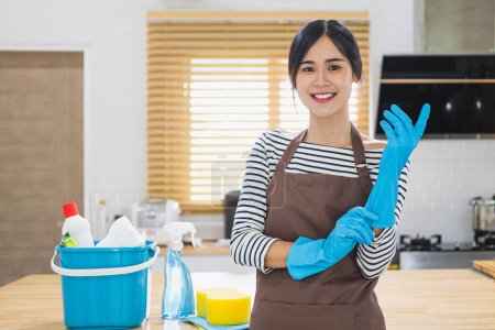 Foto de Cubo lleno de cosas clenaing casa en un escritorio de cocina con una mujer en guantes de goma. - Imagen libre de derechos