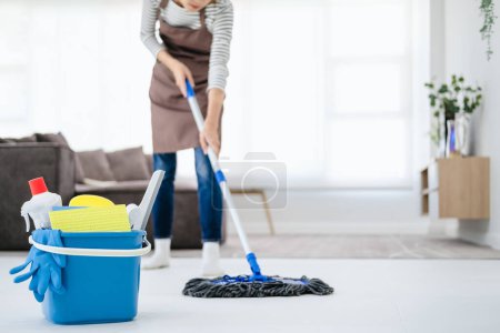 Foto de Imagen recortada de una hermosa mujer joven con guantes protectores usando una fregona mojada plana mientras limpia el piso en la casa - Imagen libre de derechos