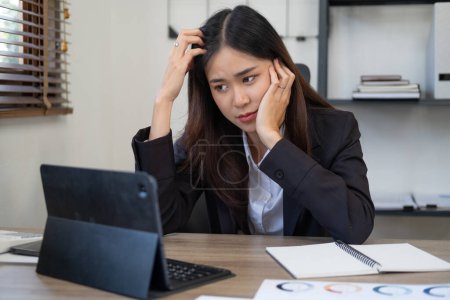 Foto de Imagen de una mujer asiática que está cansada y pensando demasiado en trabajar con una tableta en la oficina. - Imagen libre de derechos