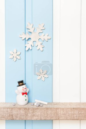 Foto de Vista frontal de muñeco de nieve y copo de nieve de madera en el estante sobre fondo azul de la pared blanca. -Decoraciones de invierno - Imagen libre de derechos