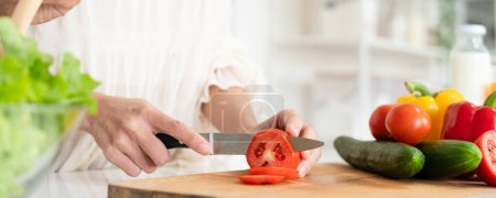 Foto de Primer plano de las manos femeninas rebanando tomate con cuchillo en tablero de madera, cocinar ensalada de verduras banner espacio de copia - Imagen libre de derechos
