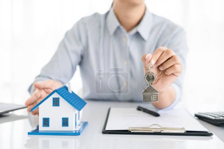 Photo for Real estate agent holding house key on house shaped keyring on table with house designs document, calculator, model house. Concept of Investment property. - Royalty Free Image