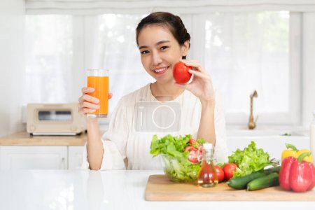 Foto de Belleza cuerpo delgado mujer asiática saludable beber vaso de jugo y tomato.young chica preparando cocinar bebida saludable con jugo de naranja fresca en la cocina en casa.Dieta concept.healthy bebida - Imagen libre de derechos
