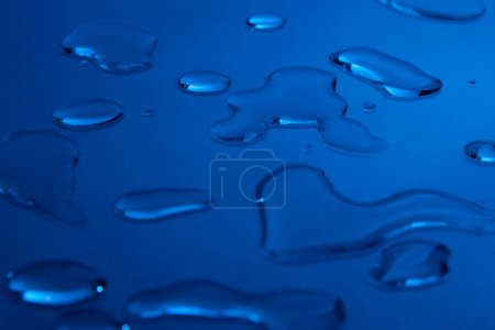 Foto de Gotas de sustancia cosmética sobre un fondo azul. Imagen de fondo para una tienda de cosméticos. - Imagen libre de derechos