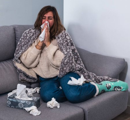 Photo for Woman feeling really sick at home sneezing surrounded by tissues - Royalty Free Image