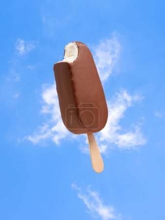 white ice cream in chocolate glaze on a stick, against the background of clouds