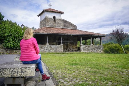 Téléchargez les photos : Jeune femme avec un manteau fuchsia contemplant l'ermitage roman de San Pelayo au Pays Basque - en image libre de droit