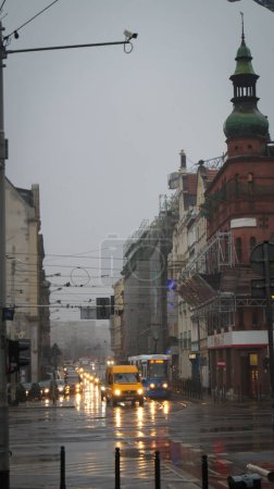 Téléchargez les photos : Des rues de Wroclaw baignées de pluie illuminent les feux des véhicules, avec des tramways qui passent et des bâtiments historiques en cours de restauration. Une caméra de surveillance surplombe la scène. - en image libre de droit