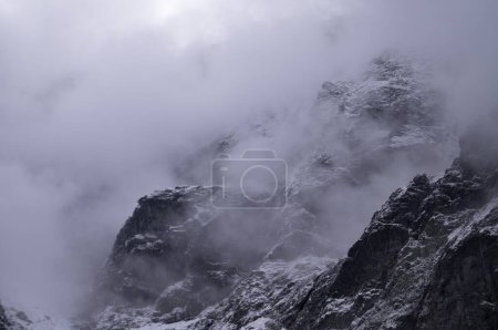 Photo for Captured in Rysy, this shot reveals the majesty of a snow-draped mountain peak, partially hidden by swirling mists. The rugged, icy surface and the ethereal fog present a stark, haunting beauty. - Royalty Free Image
