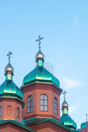 Foto de Cúpulas de tejas vibrantes y cruces ortodoxas sobre una iglesia tradicional de ladrillo en la Ucrania rural, brillando bajo la luz del sol contra un cielo azul claro. - Imagen libre de derechos