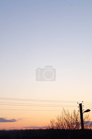 Photo for Urban sunset skyline silhouetted against a gradient sky; minimalist dusk landscape in a suburban setting, showcasing tranquil twilight with streetlamp and powerlines. - Royalty Free Image