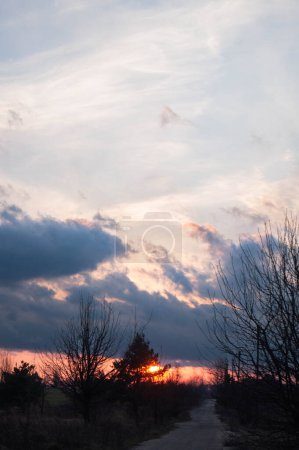 Photo for Dusk settles over a country road, sunset skies igniting clouds in nature's splendor. Rustic view along a quiet path, night embraces day. Evening's glow on rural trail, fiery sky above. - Royalty Free Image