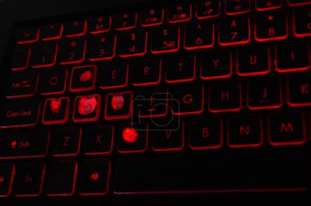 Illuminated gaming keyboard with worn keys, ideal for tech blogs and gaming setups. Backlit mechanical keyboard with signs of heavy use, perfect for articles on gaming gear durability. Red LED keyboard highlighting the reality of avid gaming.