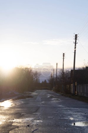 Rues grisantes au crépuscule dans une ville ukrainienne pittoresque, sous un ciel doux. L'éclat du soir adoucit le paysage rural, reflétant les allées et venues de la ville. Les teintes sombres s'installent sur une route de village enneigée, une fin de journée tranquille en Ukraine.