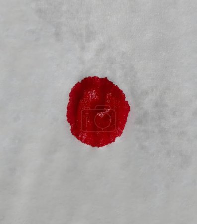 Ein einziger Tropfen rotes Blut hebt sich von einer knackig weißen Serviette ab. Starker Kontrast eines lebendigen Bluttropfens auf reinweißem Hintergrund. Das leuchtende Rot eines frischen Bluttröpfchens erzeugt ein markantes Bild auf Weiß.