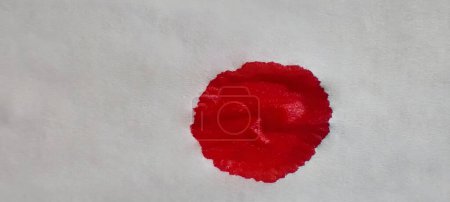 Ein leuchtend roter Blutfleck vor einem grell weißen Hintergrund. Kontrastreiches Bild, das die Schärfe eines roten Bluttröpfchens auf reinem Weiß zeigt. Die nüchterne Realität eines Bluttropfens auf Weiß, eingefangen in vielen Details.
