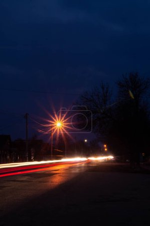 Streetlamps beam as twilight deepens, painting the road with light. Vivid streaks of car lights lace the evening streets with energy. Night descends, but the street's pulse races with glowing streams. Dusk's canvas brought to life with vibrant veins.