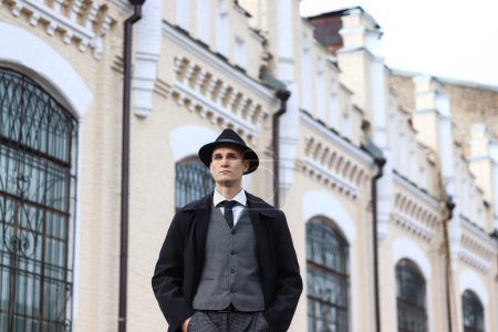 Téléchargez les photos : Séance photo pour hommes dans un costume à carreaux classique et un chapeau sur fond de vieil immeuble. - en image libre de droit