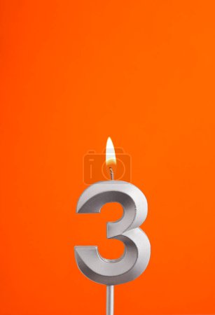 Téléchargez les photos : Numéro 3 - Bougie d'anniversaire brûlante sur fond mousseux orange - en image libre de droit