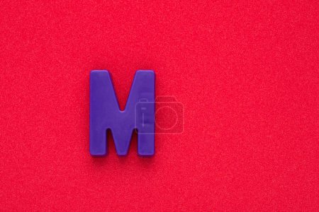 Téléchargez les photos : Alphabet lettre M - Violet pièce en plastique de couleur sur fond rouge 032 c mousse - en image libre de droit