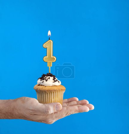 Téléchargez les photos : Livraison main cupcake d'anniversaire - Bougie numéro 1 sur fond bleu - en image libre de droit