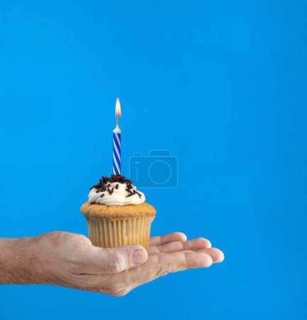Téléchargez les photos : Main tenant un cupcake au chocolat avec une bougie allumée - en image libre de droit