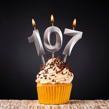 Téléchargez les photos : Bougie d'anniversaire numéro 107 - cupcake d'anniversaire sur fond noir - en image libre de droit