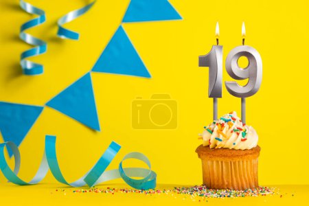 Foto de Vela de cumpleaños número 19 con cupcake - Fondo amarillo con banderines azules - Imagen libre de derechos