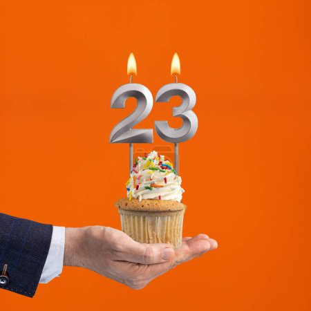 Foto de La mano que entrega cupcake con el número 23 vela - Cumpleaños sobre fondo naranja - Imagen libre de derechos