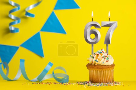 Foto de Vela de cumpleaños número 67 con cupcake - Fondo amarillo con banderines azules - Imagen libre de derechos
