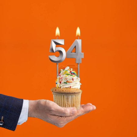 Foto de La mano que entrega cupcake con el número 54 vela - Cumpleaños sobre fondo naranja - Imagen libre de derechos