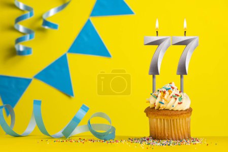 Foto de Vela de cumpleaños iluminada número 77 - Fondo amarillo con banderines azules - Imagen libre de derechos