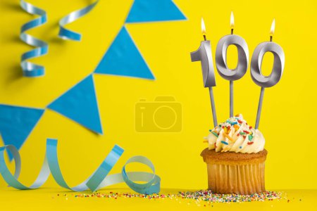 Foto de Vela de cumpleaños número 100 con cupcake - Fondo amarillo con banderines azules - Imagen libre de derechos