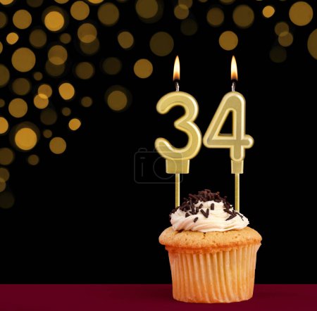 Photo for Birthday candle with cupcake - Number 34 on black background with out of focus lights - Royalty Free Image