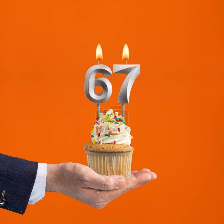 Foto de Mano celebración cupcake cumpleaños con número 67 vela - fondo naranja - Imagen libre de derechos
