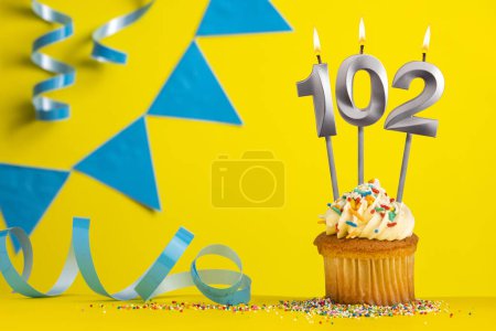 Foto de Vela de cumpleaños número 102 con cupcake - Fondo amarillo con banderines azules - Imagen libre de derechos