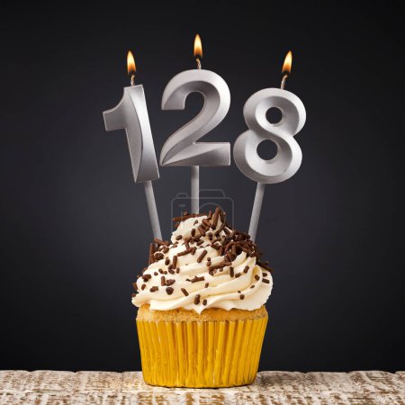 Téléchargez les photos : Cupcake d'anniversaire avec numéro 128 bougie - Célébration sur fond sombre - en image libre de droit