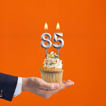 Foto de Mano celebración cupcake cumpleaños con número 85 vela - fondo naranja - Imagen libre de derechos