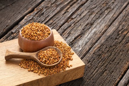 Organic fenugreek seeds in bowl and wooden spoon - Methi Dana