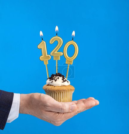 Hand delivering birthday cupcake - Candle number 120 on blue background