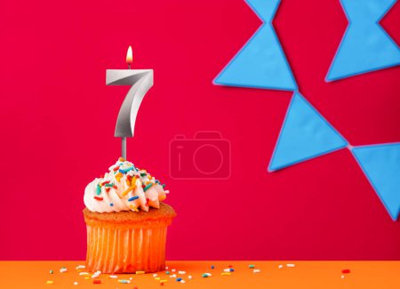 Foto de Vela número 7 con cupcake de cumpleaños sobre fondo rojo con banderines azules - Imagen libre de derechos