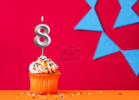 Birthday cupcake with candle number 8 on a red background with blue pennants