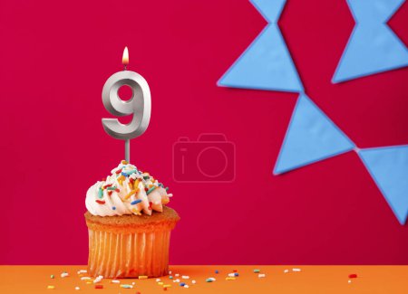 Number 9 candle with birthday cupcake on a red background with blue pennants
