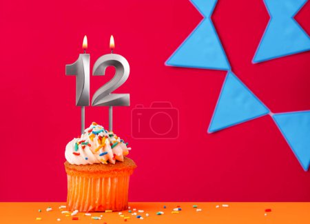 Birthday cupcake with candle number 12 on a red background with blue pennants