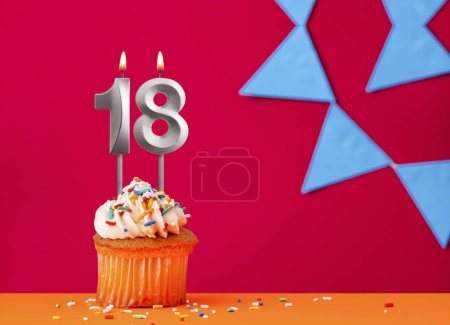Birthday cupcake with candle number 18 on a red background with blue pennants