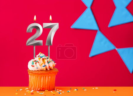 Foto de Vela número 27 con cupcake de cumpleaños sobre fondo rojo con banderines azules - Imagen libre de derechos