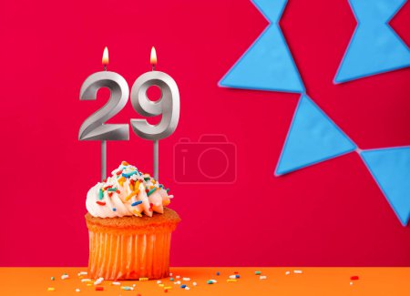 Number 29 candle with birthday cupcake on a red background with blue pennants